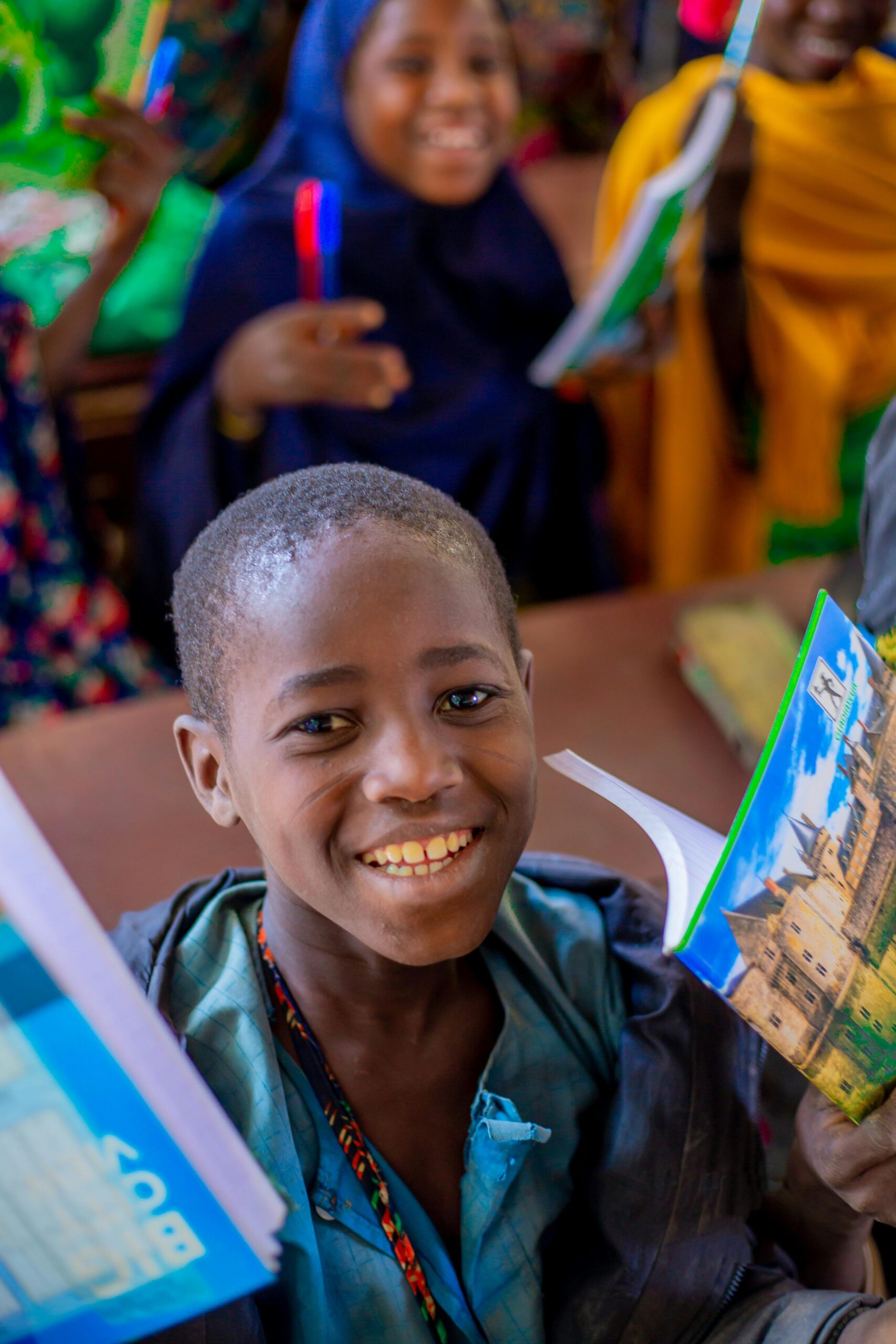 Happy African children in a classroom holding colorful notebooks and pens.
